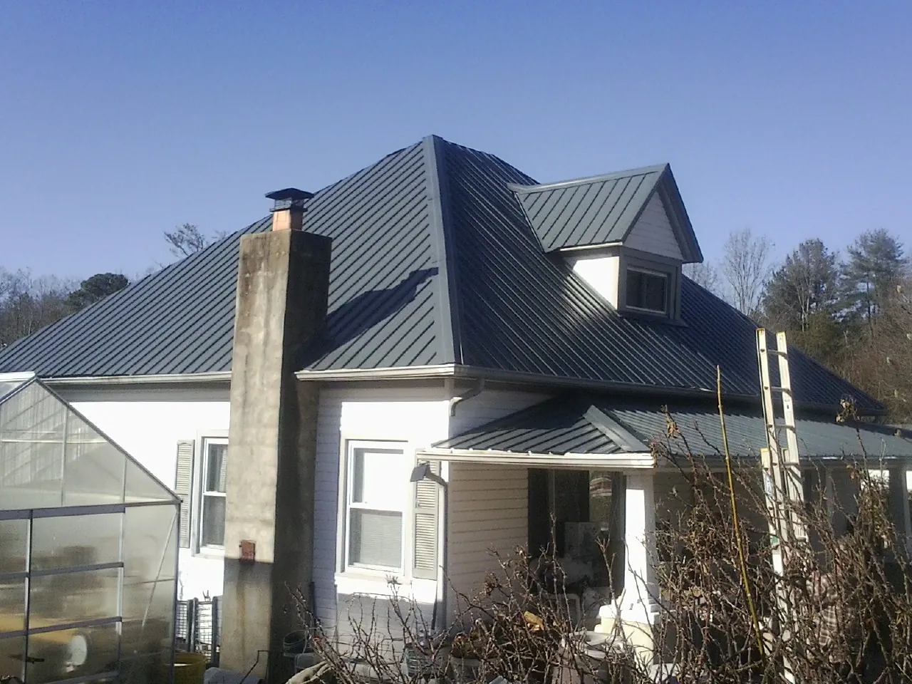 Dark blue standing seam metal roof on a white farmhouse with dormer — Slate & Tile Roof Repair by Roofing Brothers in Menomonee Falls