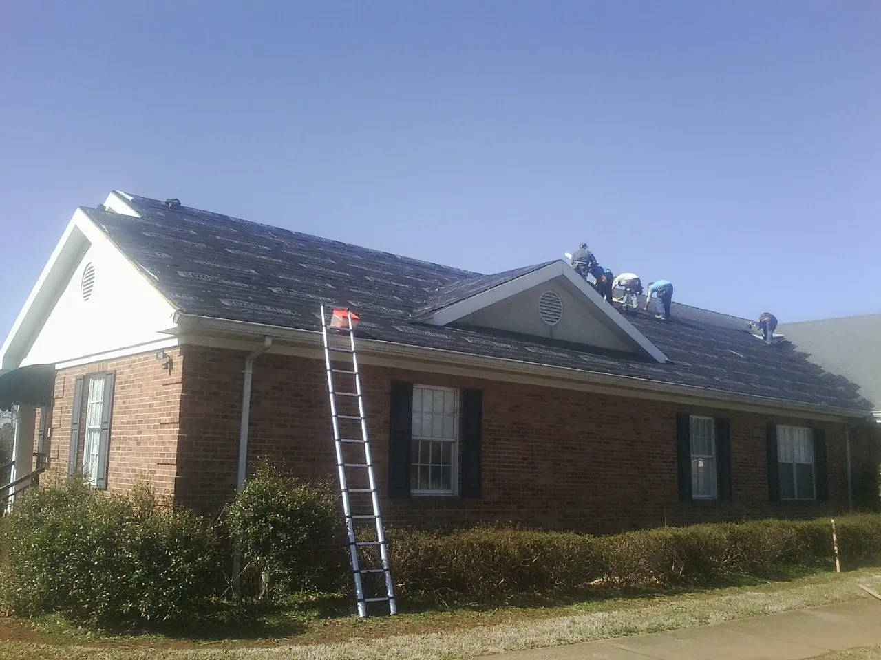 Crew tearing shingles off a brick ranch roof with a ladder set — Emergency Roof Repair work by our crew in Menomonee Falls