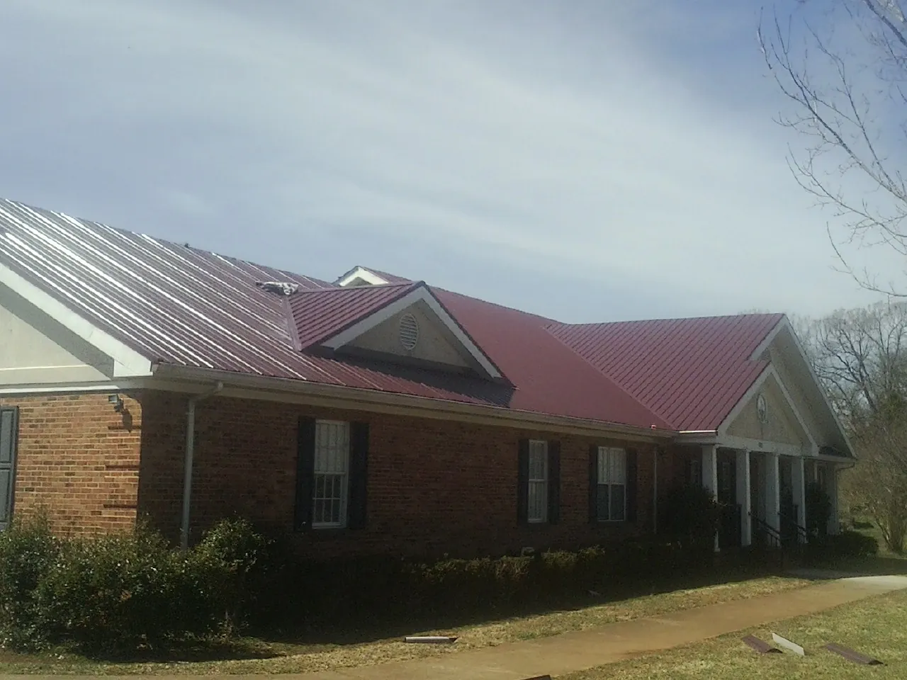 Red metal roof with gabled entries on a long brick building, from a Hail Damage Roof Repair job in Menomonee Falls