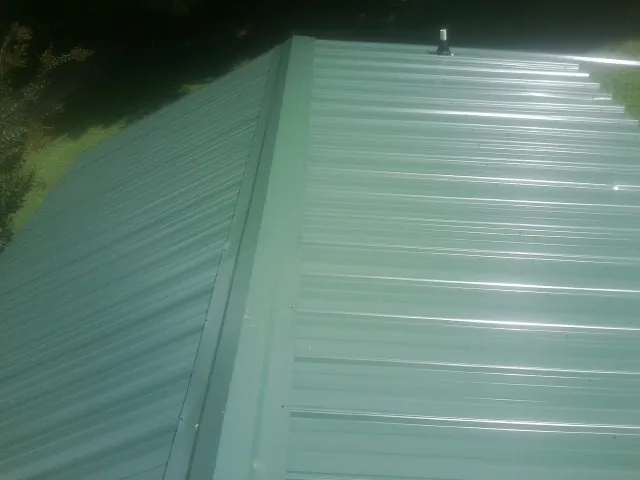 New green metal panels meeting at the ridge of a roof — Flat Roof Repair work by our crew in Menomonee Falls