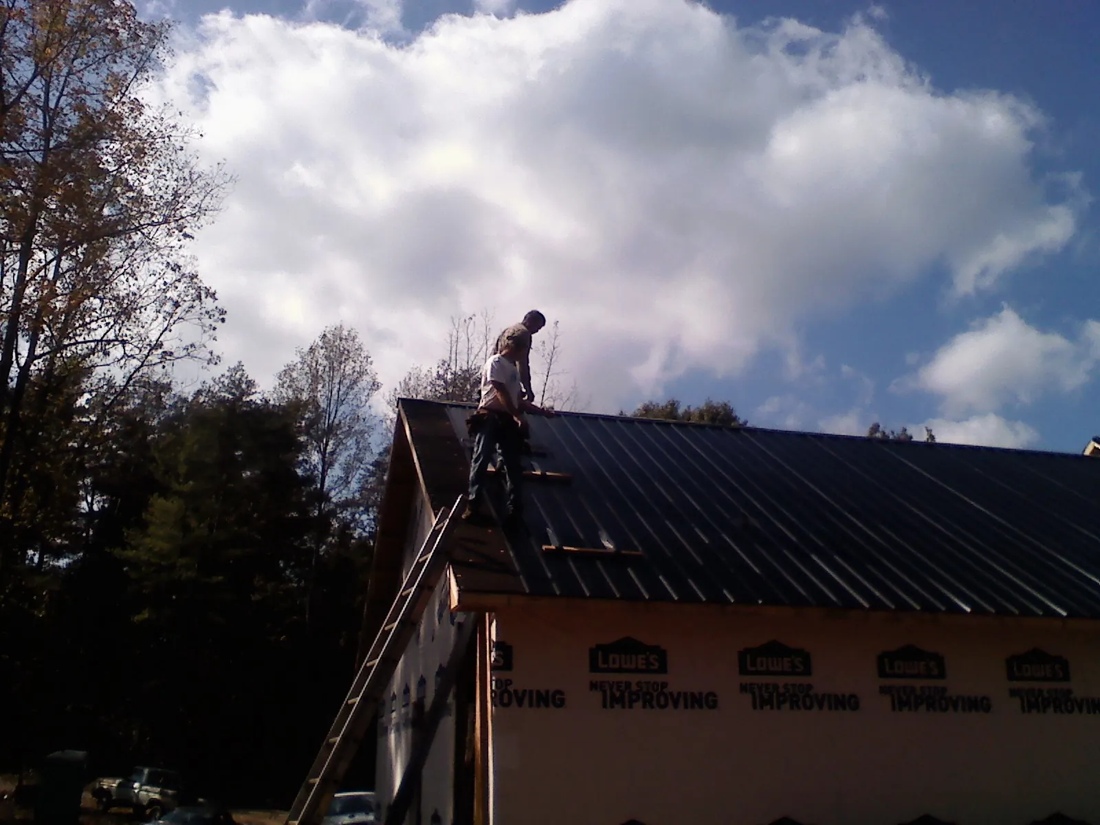 Roofer fastening dark metal panels high against a cloudy sky, from a Roof Inspection job in Menomonee Falls