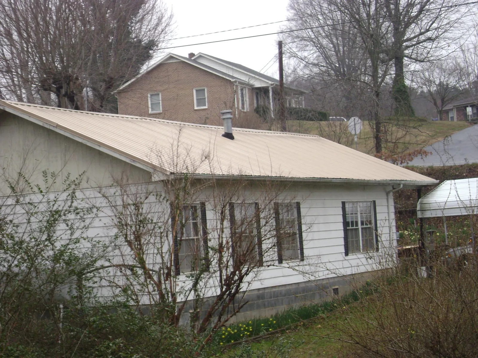 Tan metal roof on a white sided house set into a hillside — Commercial Roofing by Roofing Brothers in Menomonee Falls
