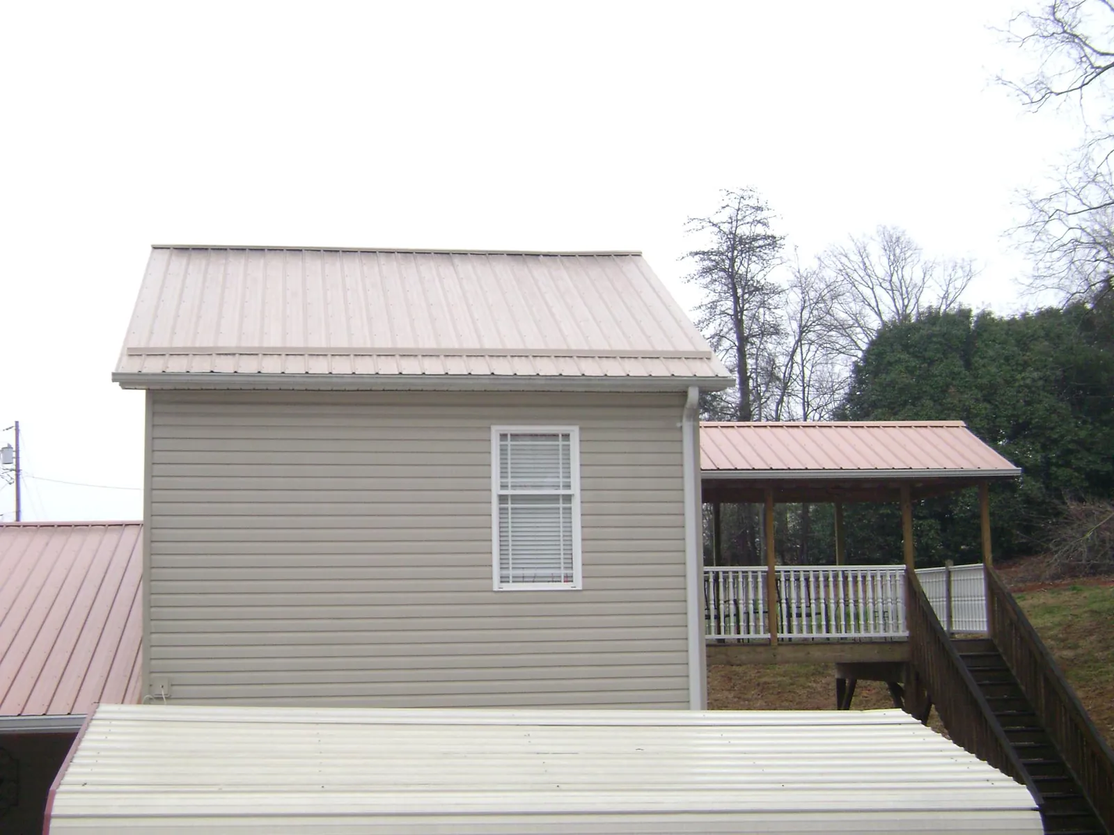 Tan metal roofs on a two story addition and attached porch, from a Roof Replacement job in Menomonee Falls